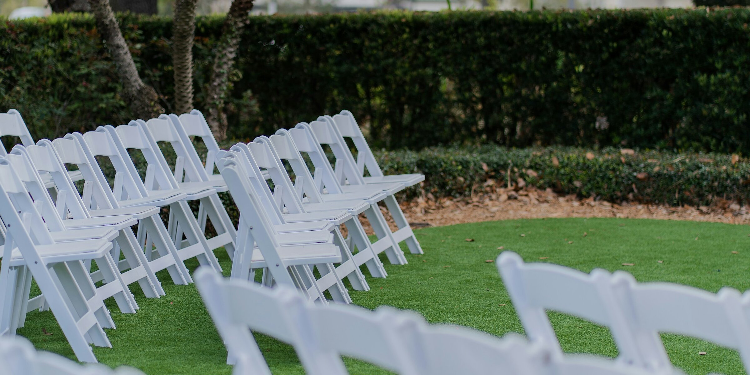 Rows of white chairs set out on a lawn for a garden ceremony